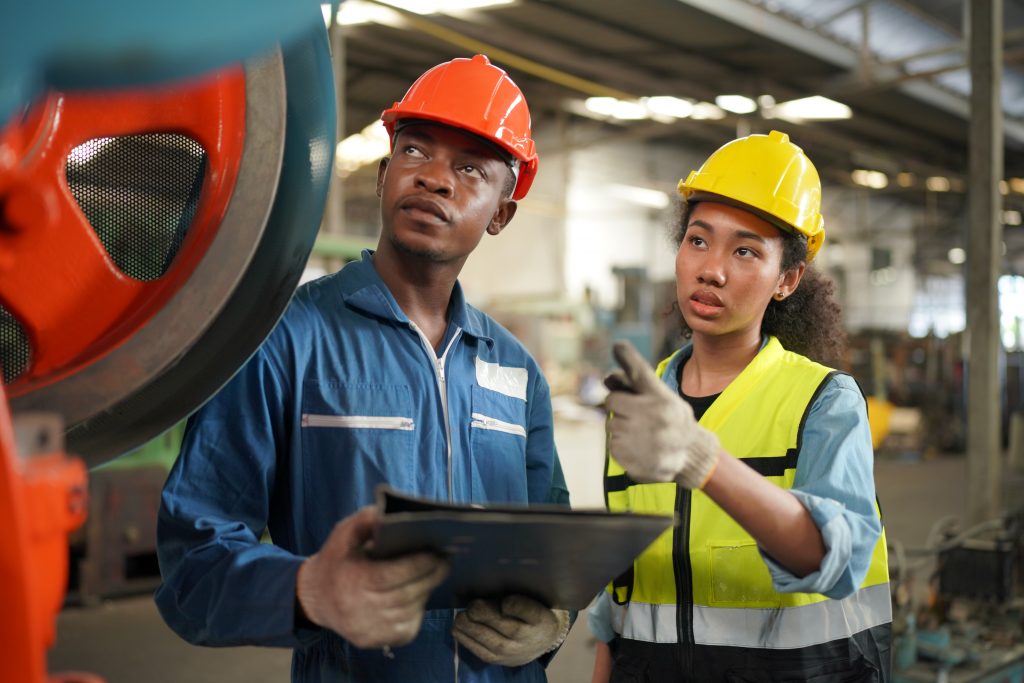 Portrait of Professional Heavy Industry Engineer / Worker Wearing Safety Uniform, Goggles and Hard Hat. In the Background Unfocused Large Industrial Factory